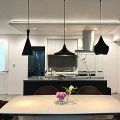 a dining room table and chairs in front of a kitchen island with lights hanging over it