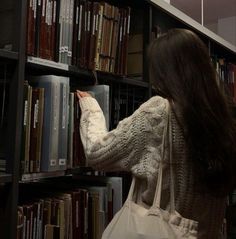 a woman is picking up some books from a book shelf in a library with other books on the shelves