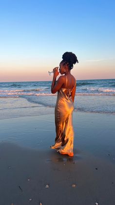 a woman standing on top of a beach next to the ocean drinking from a bottle