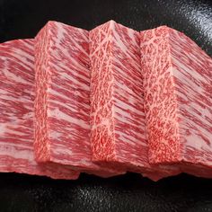 several strips of raw meat sitting on top of a black surface with red and white lines