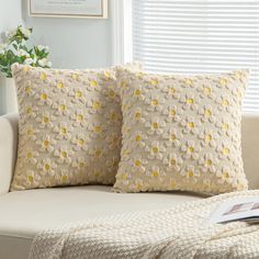 two pillows sitting on top of a white couch next to a window covered in yellow flowers