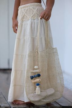 a woman holding a bag with beads and shells in it's pocket, while standing on the floor