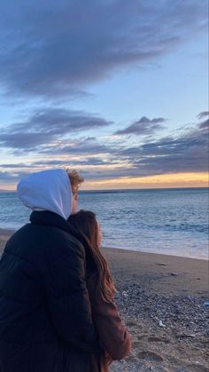 two people sitting on the beach looking at the water and clouds in the sky above them