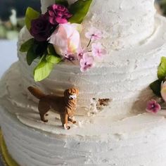 a three tiered cake with white frosting and flowers on the top, along with a small dog figurine