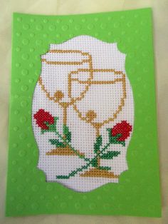 a cross stitch card with an image of two glasses and flowers on the front side