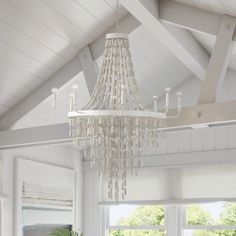 a chandelier hanging from the ceiling in a white room with windows and potted plants