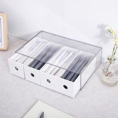 an open drawer with pens and pencils in it next to a glass vase filled with flowers