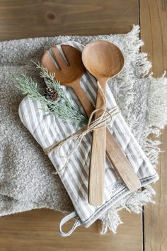 two wooden spoons on top of a towel next to a pine cone and wood utensils