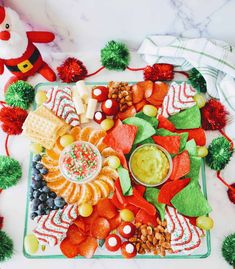 a platter filled with fruit, veggies and dip surrounded by pom - poms