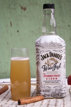 a bottle of jack daniels whiskey next to a glass filled with apple cider and cinnamon sticks