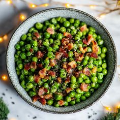 a bowl filled with peas and bacon on top of a table next to christmas lights