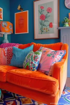 an orange couch with colorful pillows and pictures on the wall