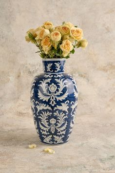 a blue and white vase with yellow roses in it sitting on a table next to a wall