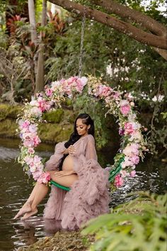 a woman in a pink dress is sitting on a swing with flowers around her neck