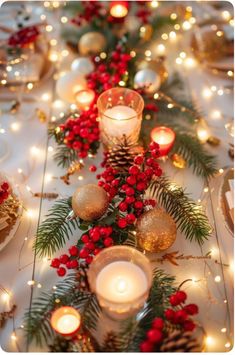 a long table with candles and christmas decorations on it, surrounded by pine cones and red berries