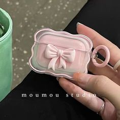 a hand holding a pink ring case with a bow on the front, and a green cup in the background