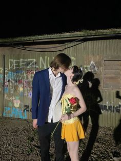 a man and woman dressed in costumes standing next to each other near a wall with graffiti on it