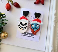 there are two earrings with faces on them next to a christmas tree and berries in the background