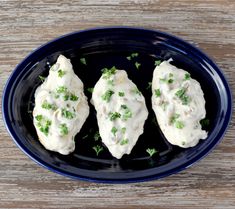 three pieces of chicken covered in white sauce and parsley on a black plate with green garnish