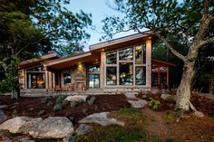 a house with large windows sitting on top of a hill next to rocks and trees