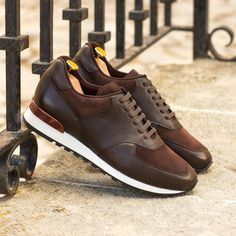 a pair of brown and white shoes sitting on top of a stone floor next to a metal fence