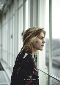 a woman standing next to a window looking out