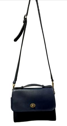 This beautiful vintage Coach Court Bag 9870 is a stylish addition to any wardrobe. Made of dark blue leather with gold hardware, it features a turn lock closure and a shoulder strap with a drop of 23-27 inches. The size of this bag is medium, with a width of 9 inches, a height of 9 inches, and a depth of 3 inches. The interior is classic vintage coach, which is unlined. So, it's blue leather inside and has one main compartment and an interior zipped pocket. There is one exterior slip pocket on the back. The bag has a square shape and a strap accent, making it a unique and fashionable accessory. Perfect for everyday use, this shoulder bag from the Coach Court collection is a must-have. Gently Pre-Owned. Remarkable condition given its age. Some minimal light wear and slight surface scratches Classic Blue Formal Flap Bag, Chic Satchel With Brass Hardware For Travel, Chic Travel Satchel With Brass Hardware, Formal Satchel Flap Bag With Hasp Closure, Classic Navy Bag For Formal Occasions, Classic Navy Formal Bag, Office Satchel Bag With Brass Hardware, Classic Blue Crossbody Flap Bag, Classic Blue Flap Bag For Everyday