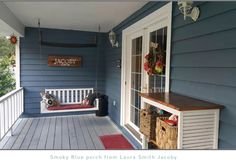 a porch with blue siding and white trim has a red rug on the wooden floor