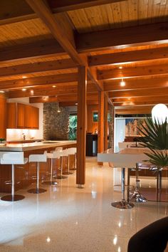 an open kitchen and living room with wooden walls, white flooring and high ceilings