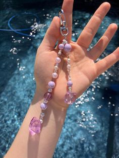 a hand holding a pink and purple beaded necklace in front of a blue pool