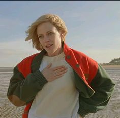 a woman standing on top of a sandy beach next to the ocean with her hands in her pockets