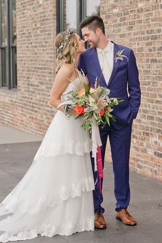 a bride and groom standing next to each other in front of a brick building