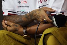 a man with tattoos on his arm and wrist sitting in a chair holding a cell phone