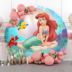 the little mermaid is sitting on top of a book surrounded by balloons and streamers