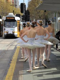 four ballerinas in white tutus waiting for the bus