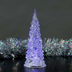 a purple glass christmas tree sitting on top of a black table next to silver and green tinsel