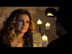 a woman singing into a microphone in front of a man with candles on the wall