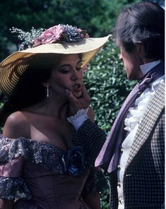 a man in a suit and hat standing next to a woman wearing a pink dress