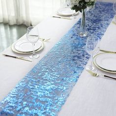 the table is set with silverware and blue sequins on the place runner