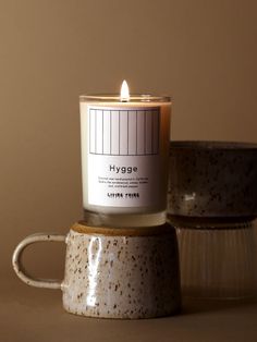 a candle sitting on top of a ceramic cup next to another one with the word hygge printed on it