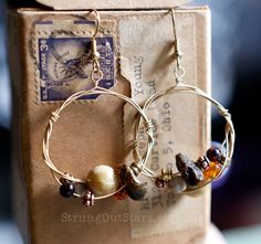 a pair of gold hoop earrings with pearls and glass beads on them sitting in front of a box