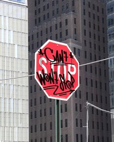 a stop sign with graffiti on it in front of some tall buildings and power lines