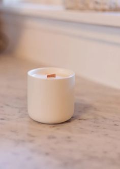 a small white cup sitting on top of a counter next to a window sill