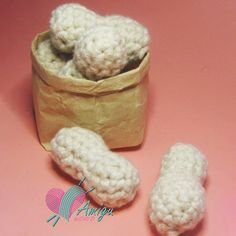 there is a small crocheted object next to a paper bag on a pink surface