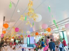 a room filled with lots of tables covered in white tablecloths and colorful paper lanterns