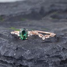 a ring with an emerald stone and diamond accents on top of a black rock in front of some rocks