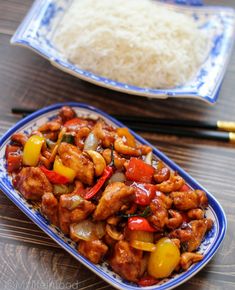 a blue and white plate topped with meat and veggies next to rice on a wooden table