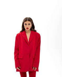 a woman is wearing a red suit and pants with her hands in her pockets,