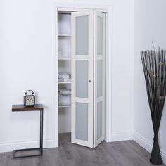 a tall white cabinet sitting in the corner of a room next to a vase with flowers