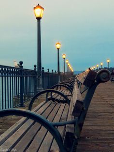 a row of benches sitting on top of a wooden pier next to the ocean at night